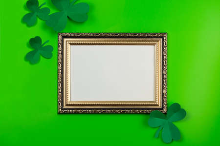 Mockup frame for photo or poster with decor for St. Patrick's Day. Blank photo frame and paper clover shamrocks on green backgroundの写真素材