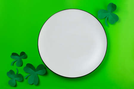 St. Patrick's empty white plate mockup. White plate and paper clover shamrocks on green backgroundの写真素材