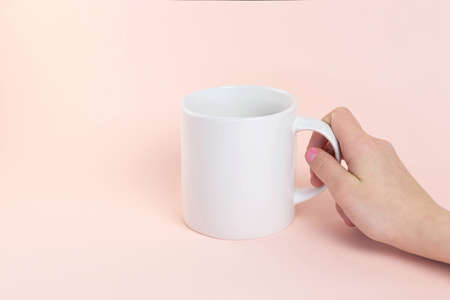 White mug mockup. Woman's hand holding mug on peach-colored background. Copy spaceの写真素材