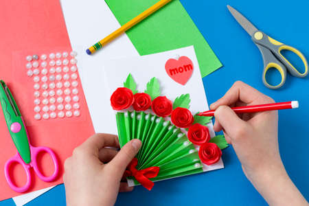 Child makes greeting card for Mother's Day. Art project for children. DIY concept. Step-by-step photo instruction. Step 16. Make inscriptionの写真素材