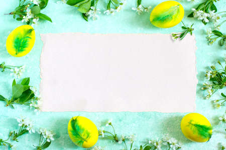 Festive Easter background with frame of bright yellow eggs with green feathers and cherry flowers...