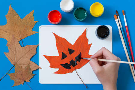 Drawing Halloween characters on dry autumn leaves. Children's art project. DIY concept. Decor for holiday party. Step 3. Draw pumpkin lanternの写真素材