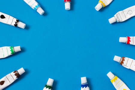 Tubes of paints on blue paper background. Frame made of tubes with multicolored paints. Flat lay, copy spaceの写真素材