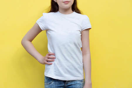 Mockup of white cotton T-shirt. Teenage girl in white T-shirt stands against yellow wall at home....