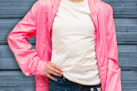 Mockup of white cotton T-shirt. Teenage girl in white T-shirt and pink jacket stands against wooden...