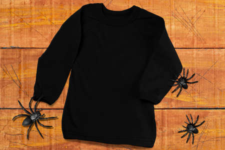 Black long sleeve t-shirt mockup. Black T-shirt on orange-brown wooden background with spiders. T-shirt mockup for Halloween design promotionの写真素材