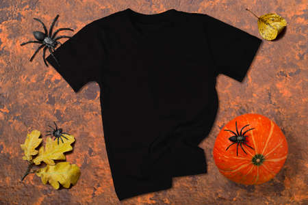 Black t-shirt mockup. Black T-shirt on orange-brown wooden background with Halloween decor. T-shirt mockup for Halloween design promotionの写真素材