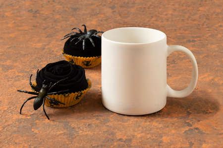 White mug mockup and funny Halloween cupcakes made of black socks with spiders. Mockup for Halloween designの写真素材