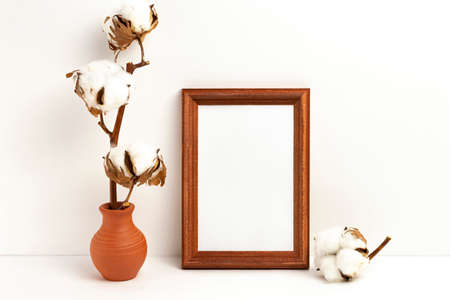 Mockup photo frame and vase with dried branch of cotton. Empty photo frame mockup to showcase your art and photo projectsの写真素材