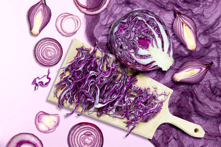 Purple vegetables on purple background. Sliced red cabbage and red onion on cutting board and purple gauze napkinの写真素材