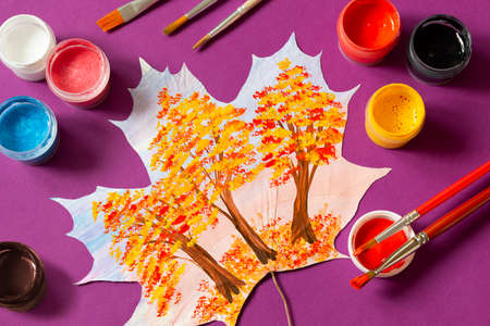 Hand-painted dry autumn maple leaves. Landscape with autumn trees on maple leaf, brushes and paints on purple background. Creative autumn art projectの写真素材