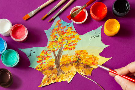 Hand-painted dry autumn maple leaves. Landscape with autumn trees on maple leaf, brushes and paints on purple background. Creative autumn art projectの写真素材