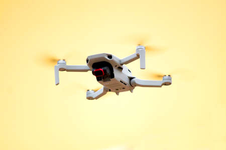 White drone quadrocopter flies against yellow wall of house and makes filming. Technology of photography of drones. Remote control. Shallow depth of fieldの写真素材