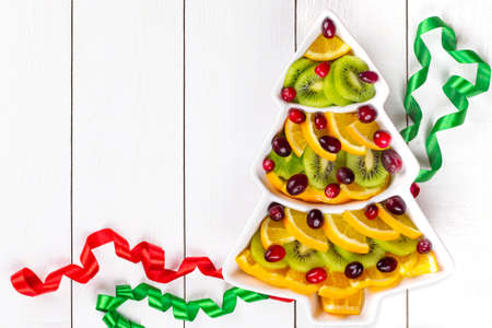 Fruit plate with slices of oranges, kiwi and cranberries in shape of Christmas tree. Minimal Christmas concept. Copy spaceの写真素材