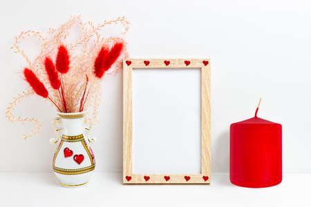 Mockup blank photo frames with Valentine's Day decor. Fluffy ornamental plants in vase, red candle...