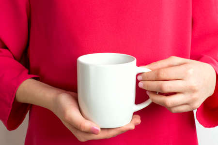 Mockup of white mug in hands of girl in red dress. Blank mug mockup for presentation and promotion designの写真素材