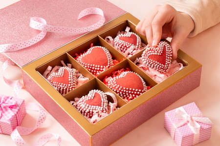 Woman's hand takes out a handmade heart-shaped gingerbread with icing from a gift box. Gifts made...
