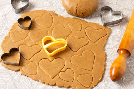 Process of making heart-shaped gingerbread for Valentine's Day. Cutting hearts out of dough with cookie cutters. Dough, rolling pin and cookie cutters on tableの写真素材