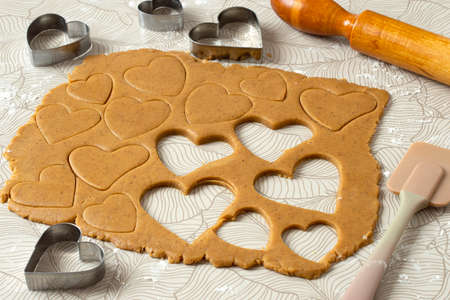 Process of making heart-shaped gingerbread for Valentine's Day. Cutting hearts out of dough with cookie cutters. Dough, rolling pin and cookie cutters on tableの写真素材