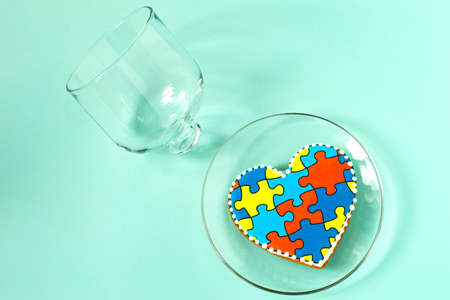 Heart shaped gingerbread covered with multicolored glaze with pattern of puzzles and glass cover lying separately. concept of autism. Help in interacting with outside world. World Autism Awareness Dayの写真素材