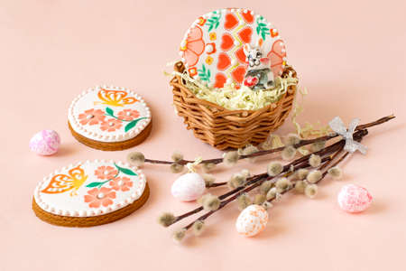 Colorful painted Easter egg-shaped gingerbread in basket and on table. Gingerbread cookies are covered with sugar glaze with beautiful color patterns. Decorative pink eggs and willow branchesの写真素材