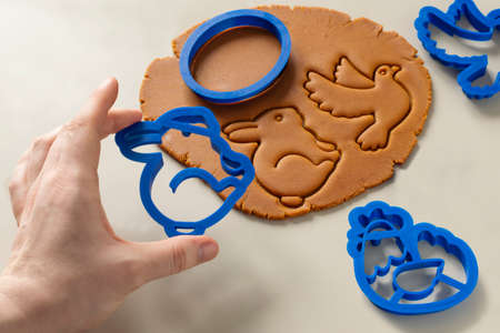 Women's hands cut Easter gingerbread from dark honey dough with spices. Thematic cookie cutters for Easter bunny, egg, dove, chicken are used. close-upの写真素材