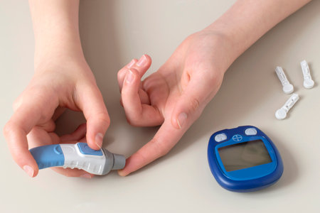 Girl injects herself with automatic lancet to measure her blood glucose level. Portable glucometer for taking measurements at home with test strip and lancets on tableの写真素材