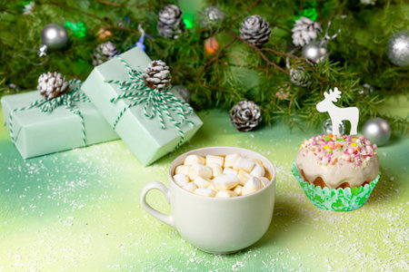 Hot chocolate with marshmallows, festive muffin with icing and multicolored sugar sprinkles, Christmas gifts and Christmas garlandの写真素材