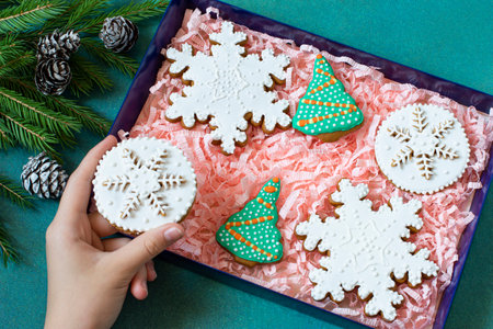 Hand of girl holding Christmas gingerbread covered with icing with pattern in shape of snowflake. Variety of festive Christmas gingerbread made of honey dough with spices covered with icing in boxの写真素材