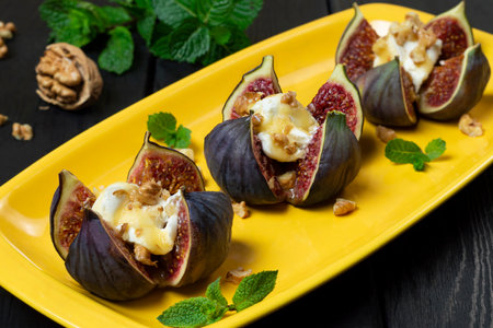 Ripe figs stuffed with cream cheese with honey sauce and walnuts on bright yellow plate. Delicious appetizer, perfect aperitif or fruity dessertの写真素材