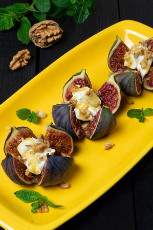 Ripe figs stuffed with cream cheese with honey sauce and walnuts on bright yellow plate. Delicious appetizer, perfect aperitif or fruity dessertの写真素材