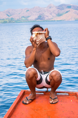 A man sitting at the boat and  blowing on a conch shell at Coron island Philippinesの写真素材