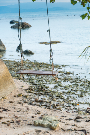 Empty wooden swing on an exotic beach - Phangan island, Thailand. Wodden swing tied with ropes to a tree with sea in the background.の写真素材