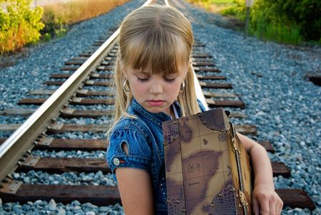 Sad little girl with suitcase on railroad track.の写真素材