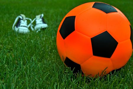 Orange soccer ball with sneakers on playing field.の写真素材