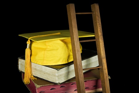 Ladder leaning against stack of old books with graduation cap.の写真素材