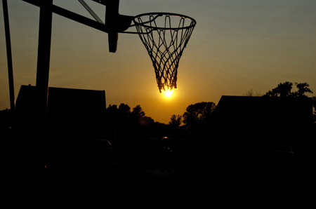 silhouette of basketball hoop with sun at sunset