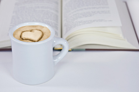 cup of cappuccino with heart design and open bookの写真素材