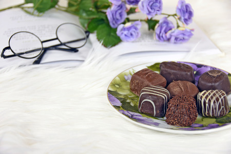 fancy chocolates on plate with book and roses on white furの写真素材