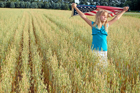 young girl in wheat field with American flagの写真素材