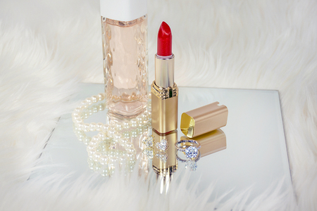 red lipstick with perfume bottle on mirror with diamond ring and pearl necklaceの写真素材