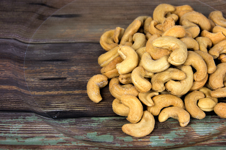 pile of salted cashews on rustic wood grain plateの写真素材