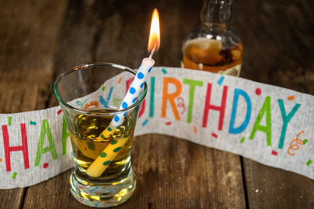 Birthday candle in shot glass with whiskey on rustic woodの写真素材