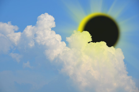 Near total eclipse of the sun behind fluffy cloud