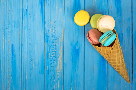 colorful macaroon cookies in waffle cone on blue painted woodの写真素材