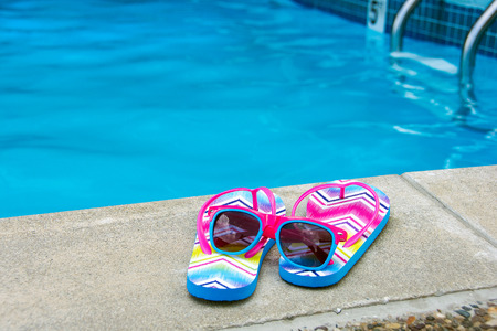 sunglasses on flip-flops by swimming pool edgeの写真素材