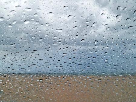 Raindrops on window with beach and stormy sky blurred backgroundの写真素材