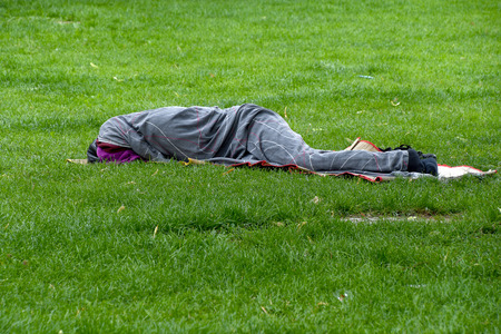 sleeping homeless man wrapped in gray blanket on green grassの写真素材