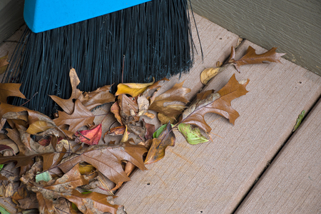 dried autumn leaves with broom on wooden deckの写真素材