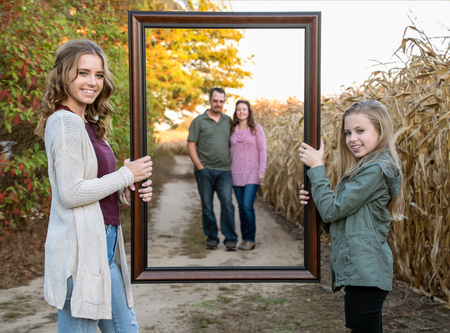 blond sisters holding picture frame of parents blurred in background on dirt roadの写真素材